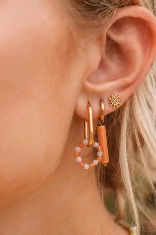 Ovale oranje hoepel oorringen met parels en gouden kralen op oor met meerdere piercings